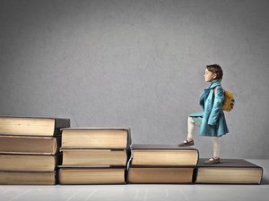 Der Weg der Bildung. Foto: Adobe Stock/Olly Mädchen steigt eine Büchertreppe hoch.
